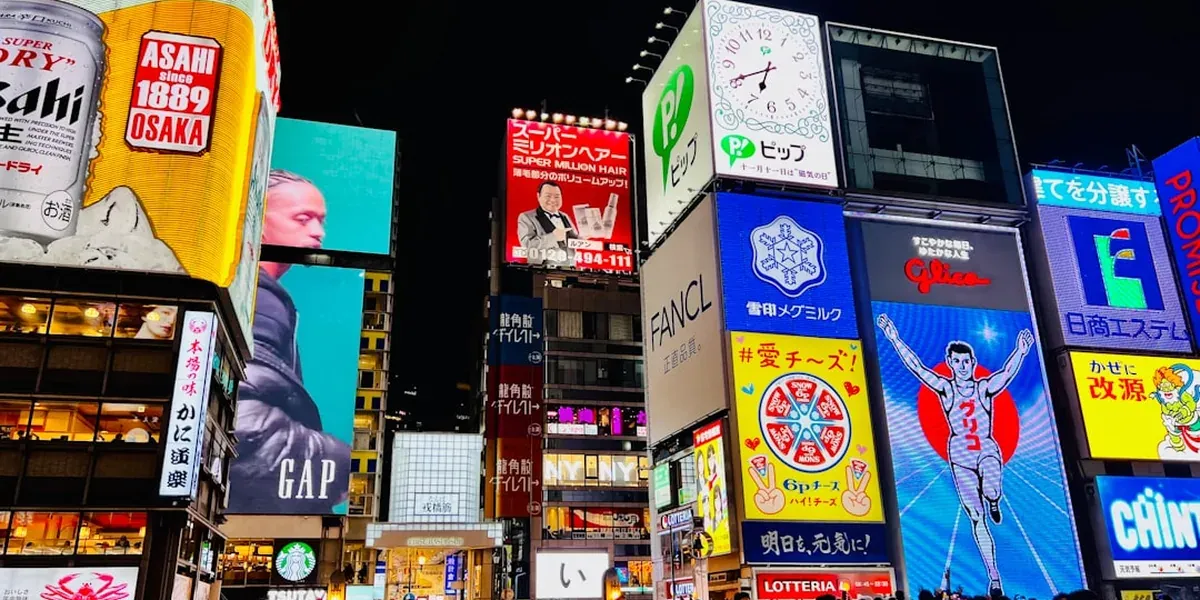 Busy Namba/Dotonbori street in Osaka at night with neon signs, food stalls, and crowds