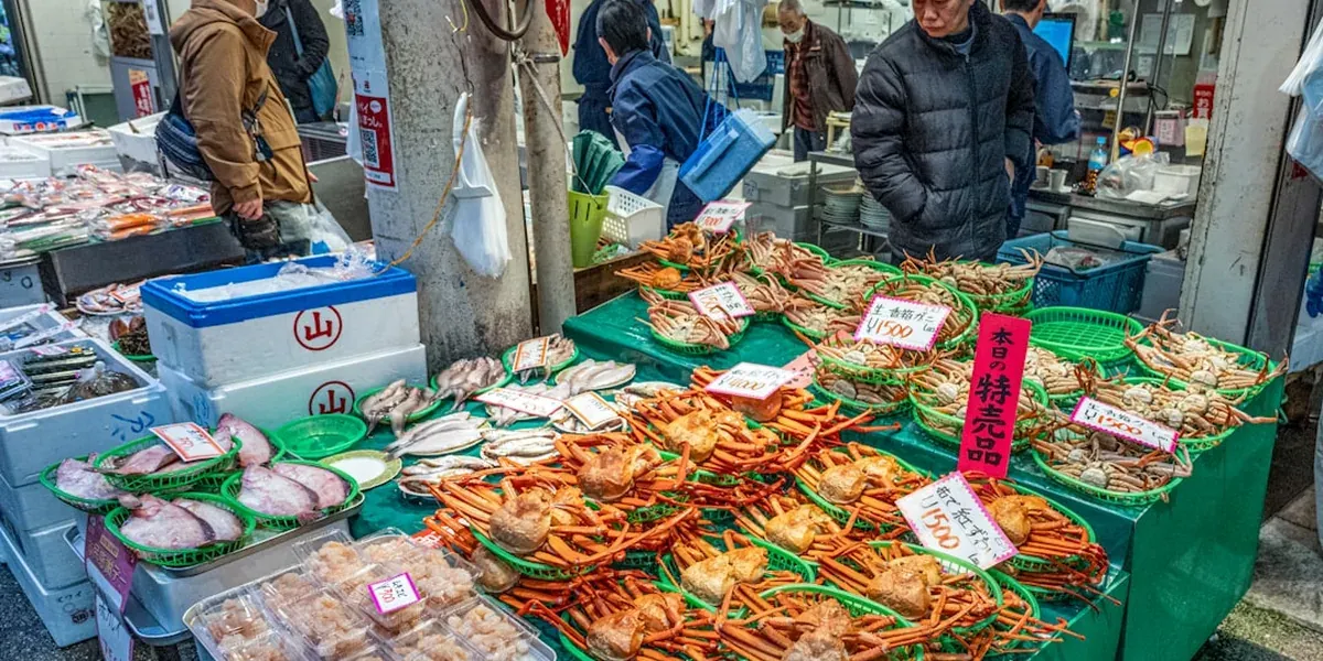 Omicho Market in Kanazawa with fresh seafood displays including crab, shrimp, oysters, and yellowtail fish on ice at vendor stalls