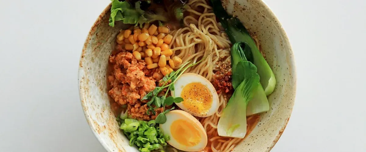 A bowl of Okinawa soba with wheat noodles in clear pork-bone broth, sliced pork, fish cake, and green onions