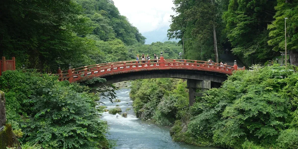 The red-lacquered Shinkyo Sacred Bridge spanning the Daiya River in Nikko with mountains in the background