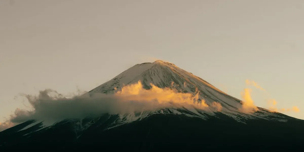 The summit of Mt Fuji at sunrise with clouds below the peak