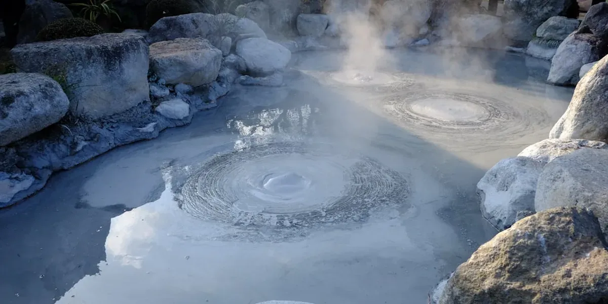 A traditional Japanese outdoor onsen (hot spring) with steam rising and mountains in the background