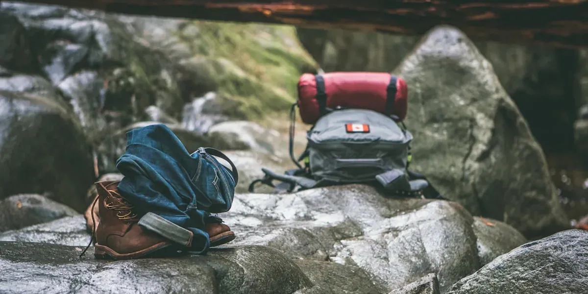 Hiking gear laid out: boots, backpack, water bottle, and rain jacket